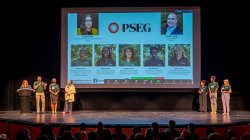 Seven people stand on stage in front of a large screen with the acronym PSEG and photos of team members.