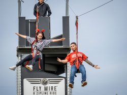 A young woman and young man are harnessed in a zip line and speed toward the camera.
